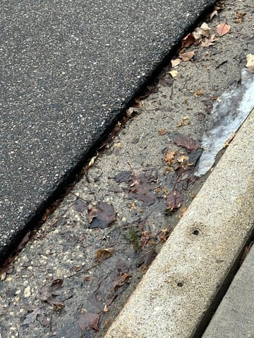 Frost heave lifting asphalt near curb in Minnesota during seasonal freeze thaw